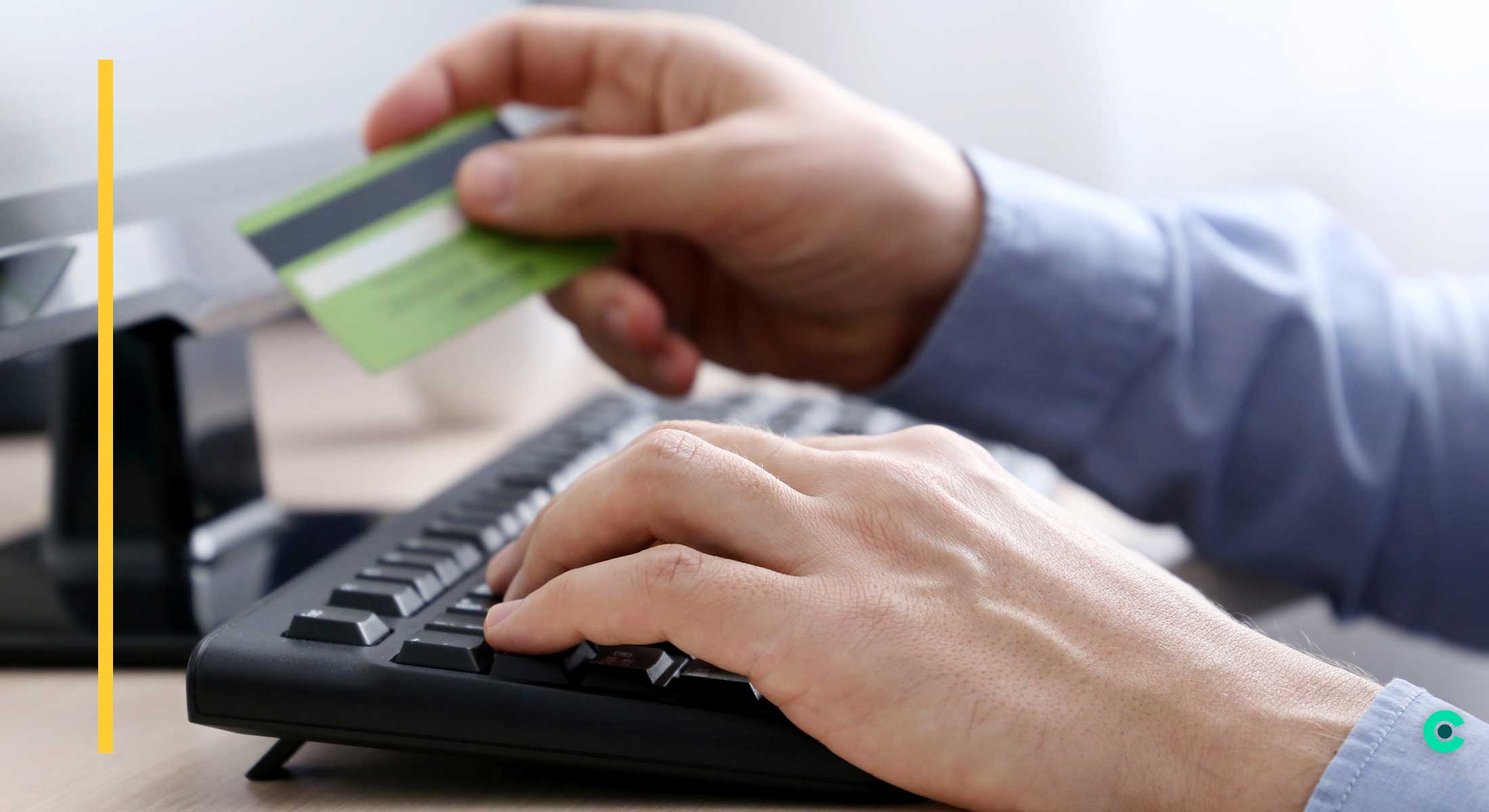 A man holds a credit card above a keyboard