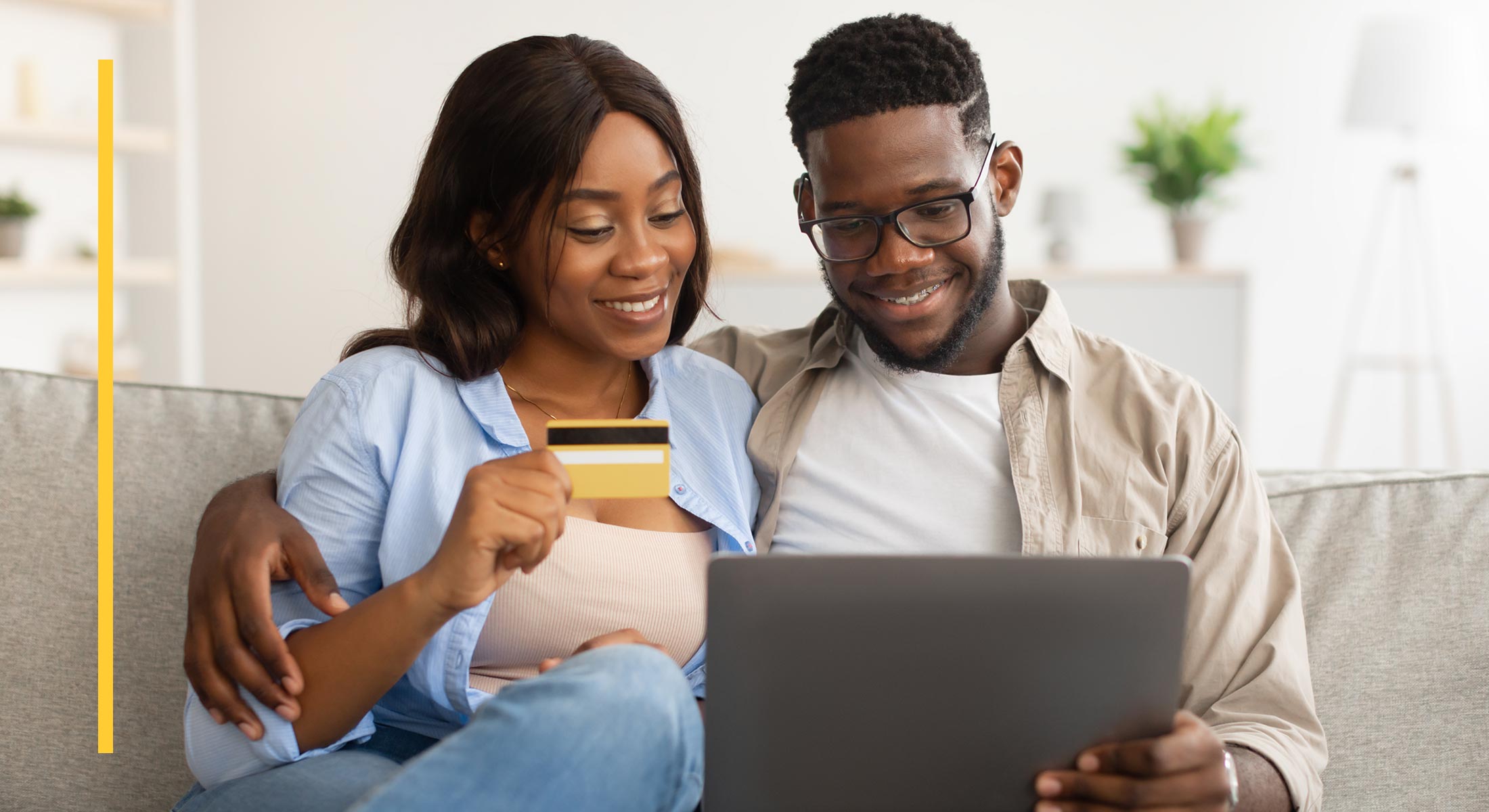 A couple sits on a sofa with credit card and sofa, ready to make a purchase