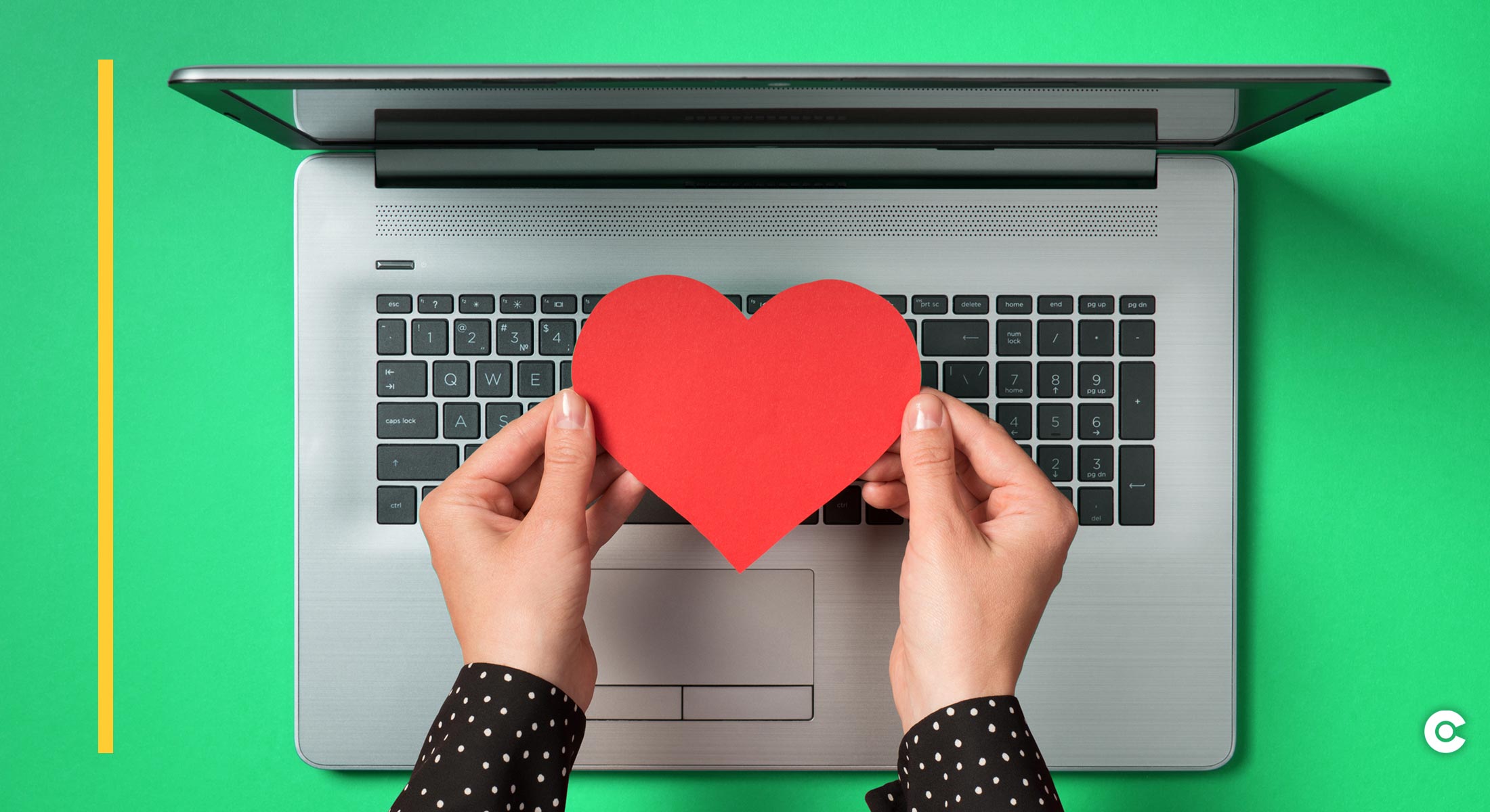 Two hands hold a cut-out of a red heart above a laptop keyboard
