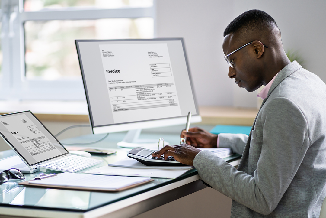 A person at a desk reviewing an invoice on a computer.